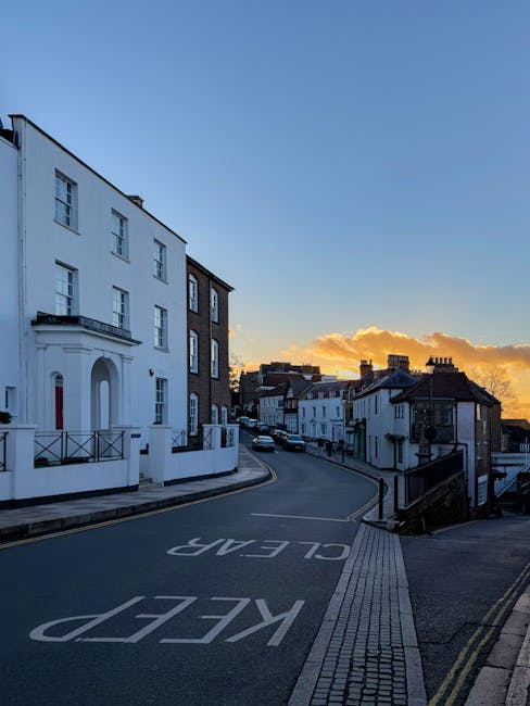 A steep residential street in an urban area with multicoloured Victorian-style terraced houses on each side, featuring bay windows, decorative cornices, and small front gardens. The street is paved wi